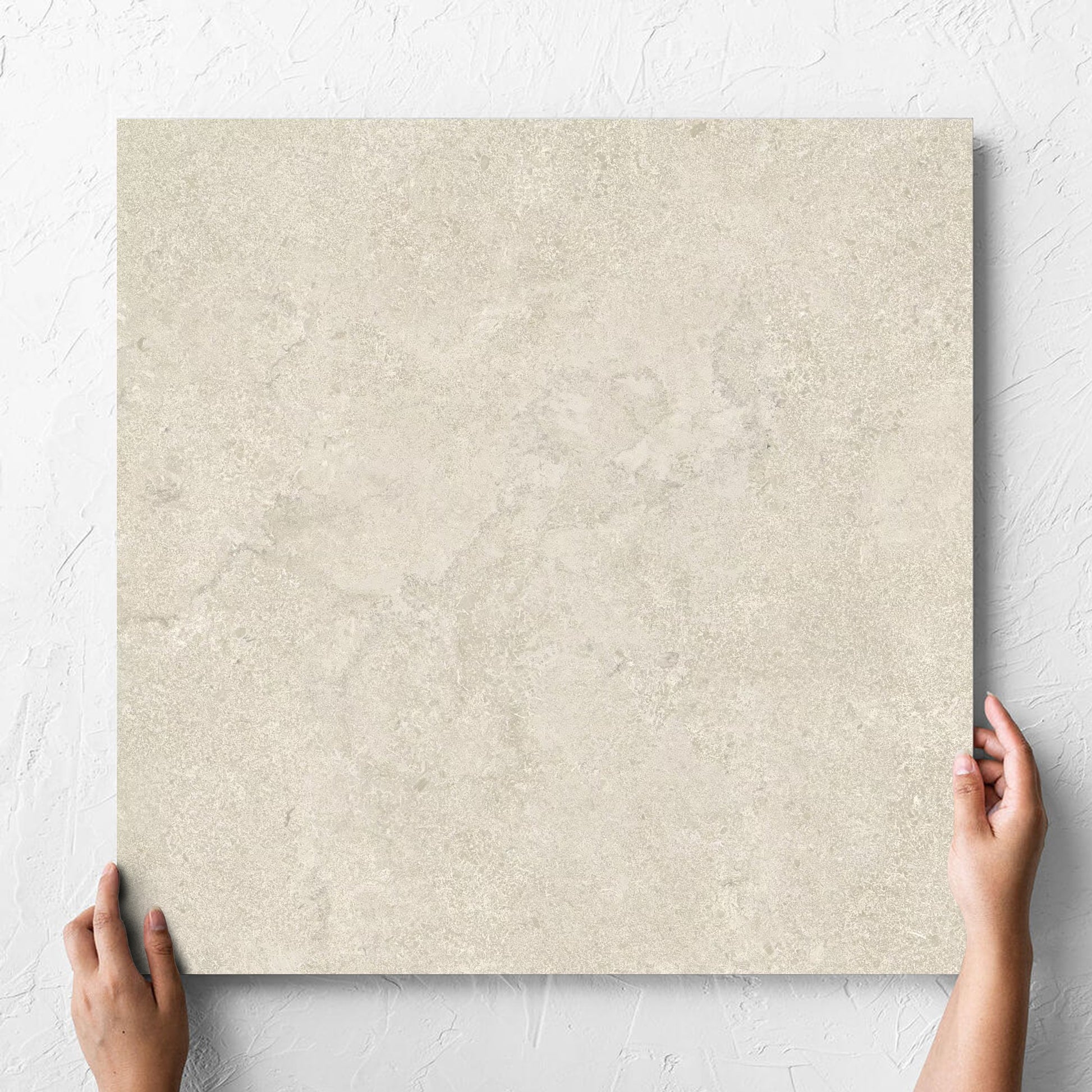Hand holding a single Roman Travertine Beige 600x600mm tile against a white rendered wall, showing the beige matt surface