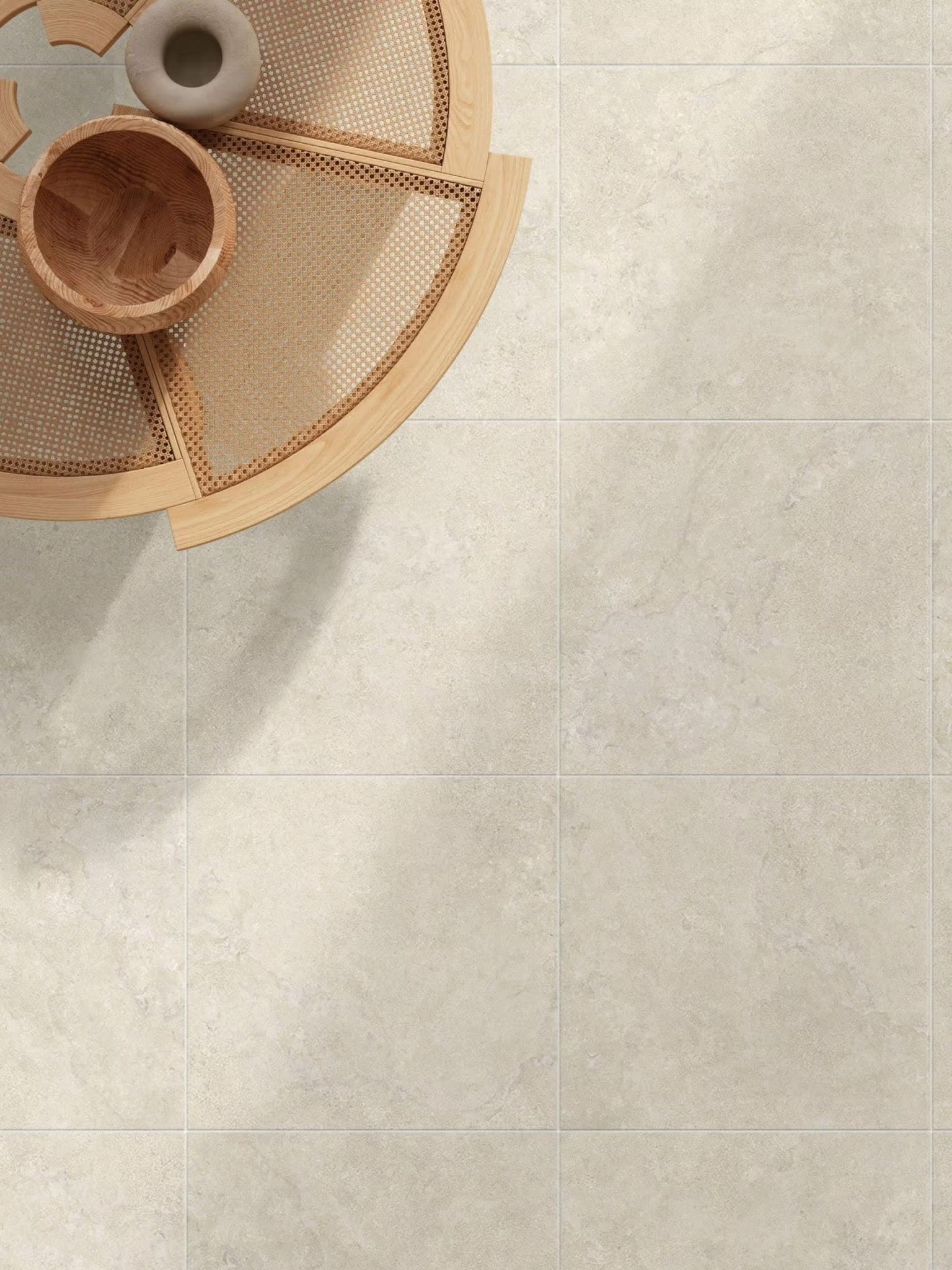 Roman Travertine Beige 600x600mm floor tiles in a living room styled with a round rattan coffee table and wooden decorative bowls.