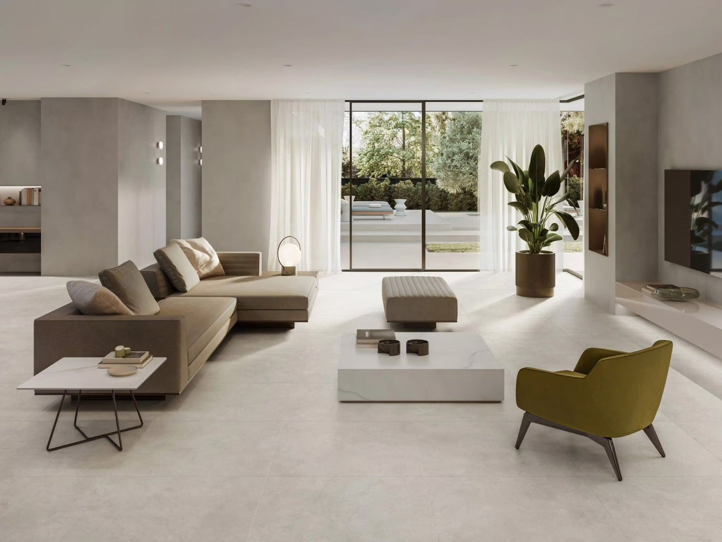 Roman Travertine Beige 600x600mm tiles laid across a bright open-plan living room floor with sectional sofa, olive armchair, and floor-to-ceiling glazed doors.