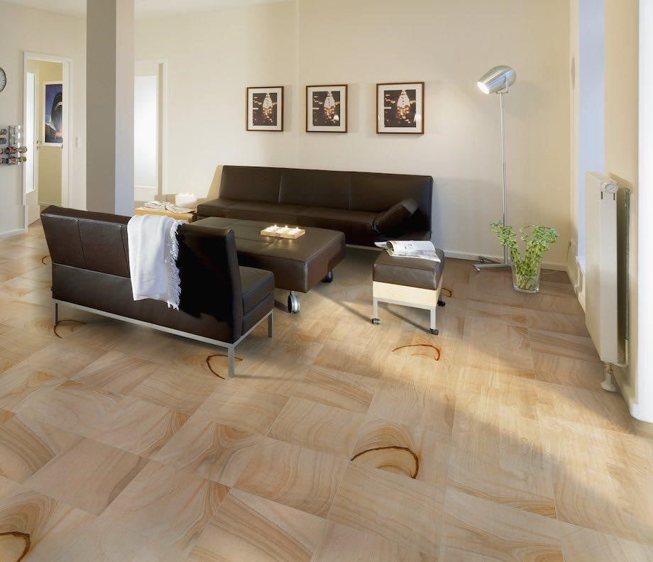 Sand Spa Beige 300x600mm tiles installed as a herringbone-style living room floor, complementing dark leather sofas and a floor lamp.