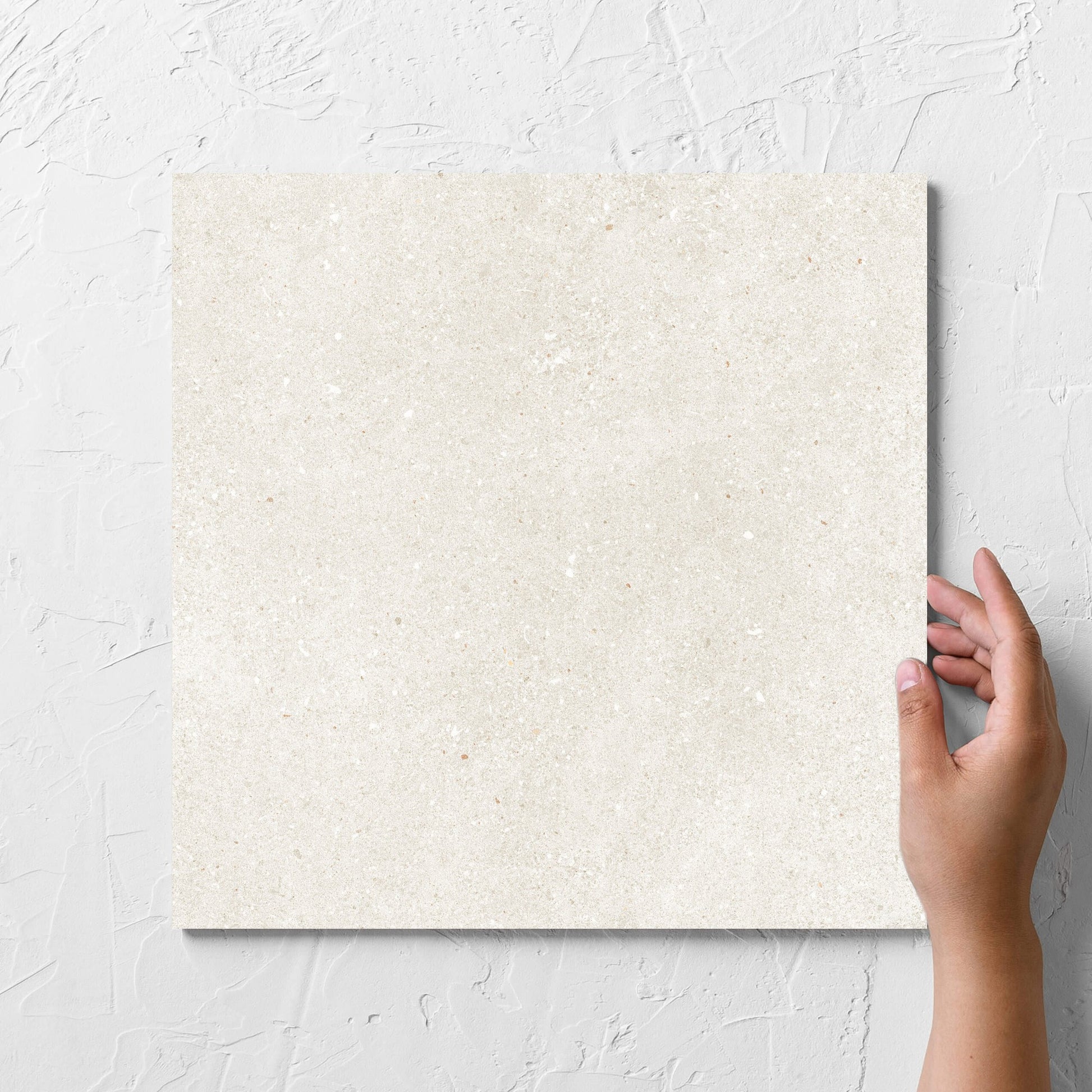 Hand holding a single Serenity Beach Sand 300x300mm tile against a white rendered wall, showing the matt surface