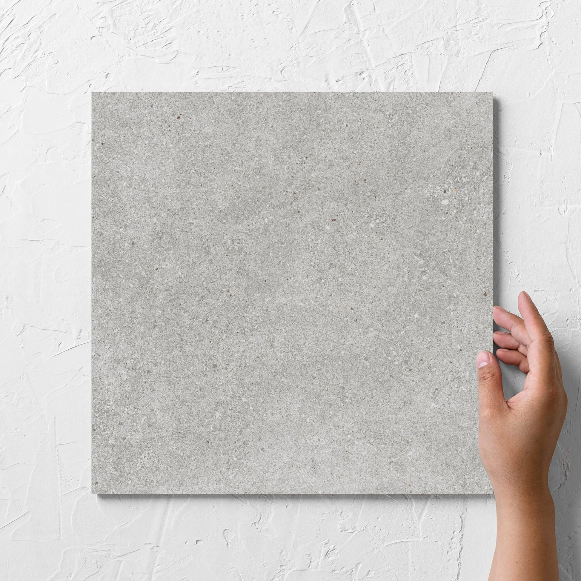 Hand holding a single Serenity Concrete Grey 300x300mm tile against a white rendered wall, showing the matt surface