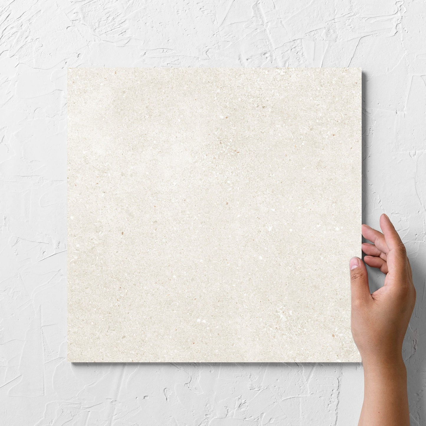 Hand holding a single Serenity Light Mocha 300x300mm tile against a white rendered wall, showing the matt surface