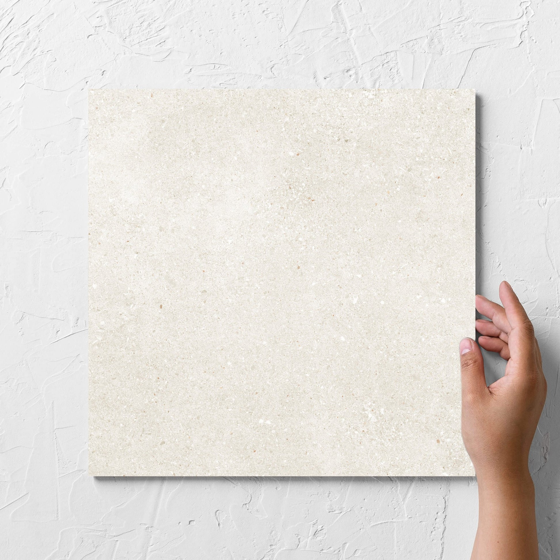 Hand holding a single Serenity Light Mocha 300x300mm tile against a white rendered wall, showing the matt surface