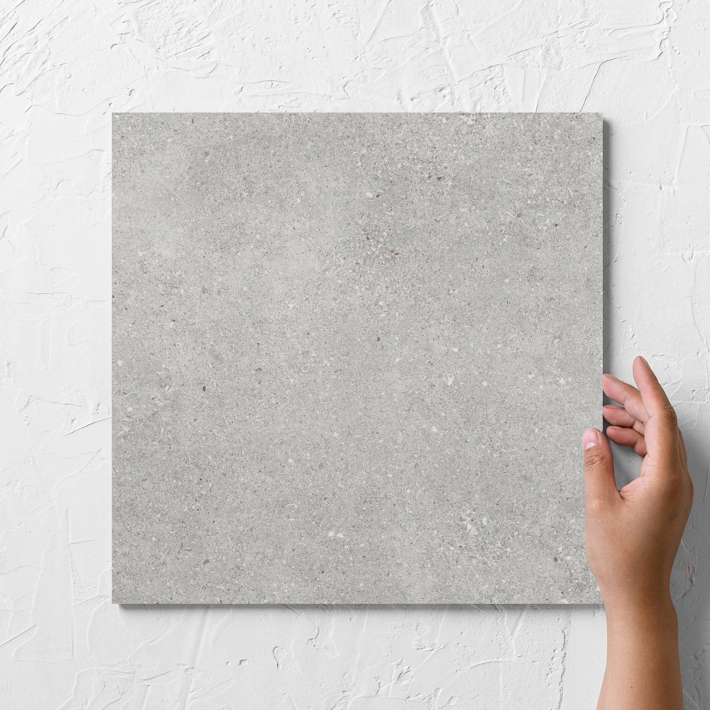 Hand holding a single Serenity Urban Stone 300x300mm tile against a white rendered wall, showing the matt surface