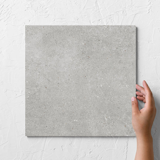 Hand holding a single Serenity Urban Stone 300x300mm tile against a white rendered wall, showing the matt surface