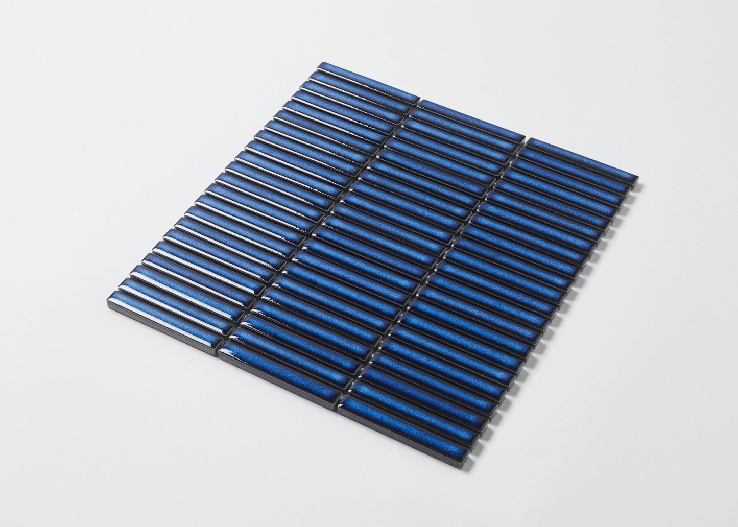 A flat-lay pack shot of Shadow Blue Gloss Porcelain Glazed KitKat 12x92mm tiles arranged in a mesh-mounted sheet with a glossy, cobalt-blue ribbed finish.