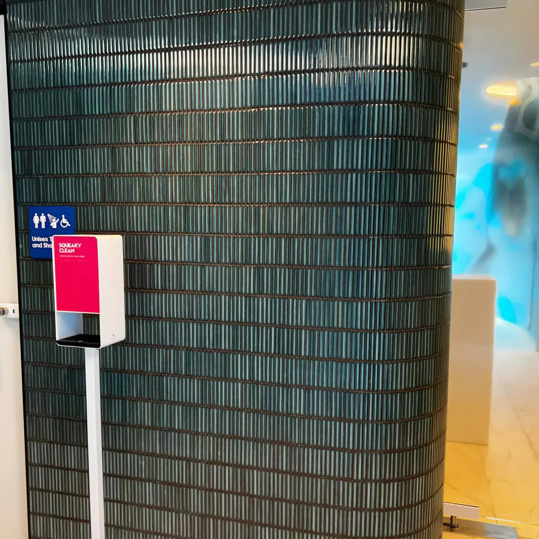 Shadow Dark Green Gloss Porcelain KitKat 12x92mm tiles installed on a curved teal column beside a unisex bathroom sign and hand sanitiser station.