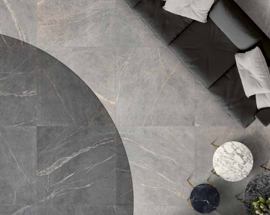 Soap Stone Grey 600x600mm porcelain floor tiles installed in a luxury living room with a curved dark inlay pattern, sofa, and marble side tables viewed from above.