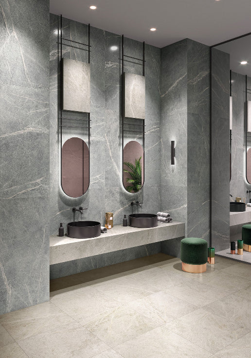 Soap Stone Grey Honed 600x1200mm tiles covering floor-to-ceiling bathroom walls beside a floating double vanity with black vessel sinks and oval mirrors.