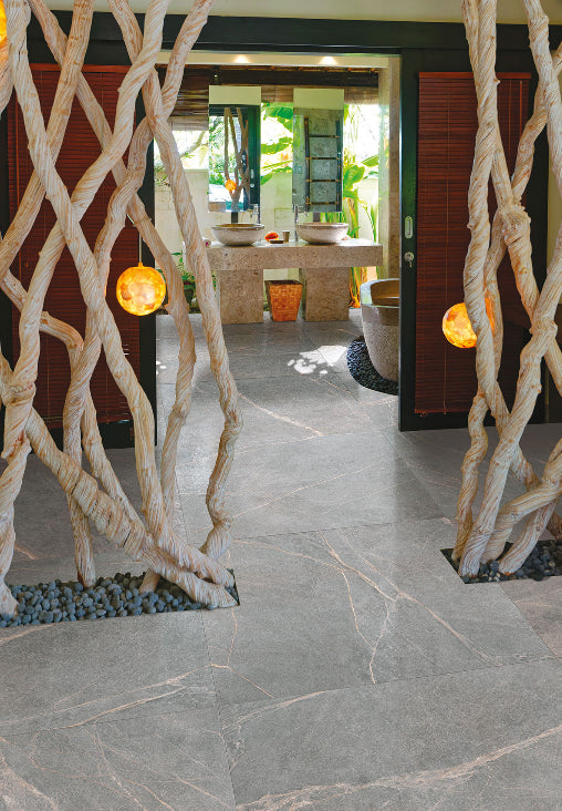 Soap Stone Grey Honed 600x1200mm tiles laid on a resort entryway floor flanked by sculptural driftwood columns with warm glowing amber lights.