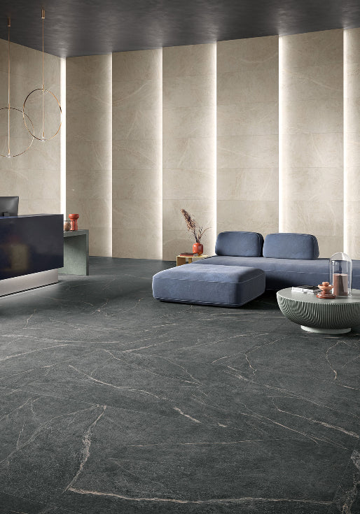 Soap Stone White External 600x600mm tiles installed as a dark marble-effect floor in a modern living room with blue modular sofa and illuminated wall panels.