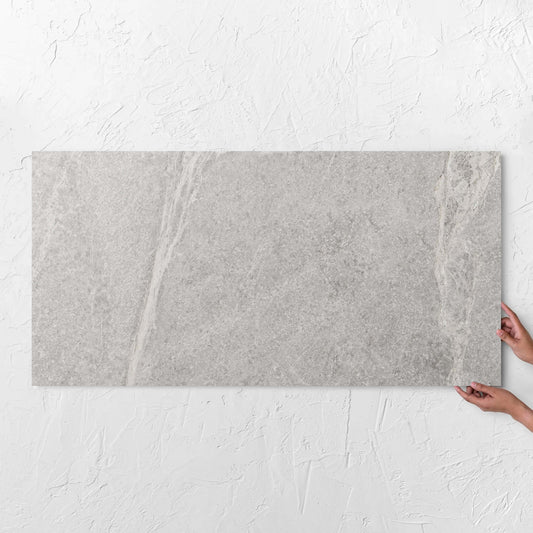 Hands holding a Soap Stone White Honed 600x1200mm tile against a white rendered wall, showing the tile surface