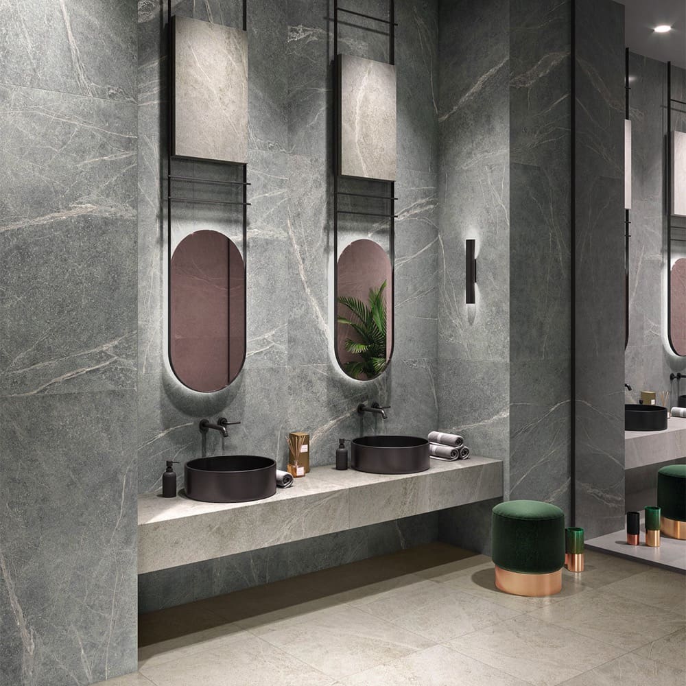 Soap Stone White Honed 600x1200mm tiles installed as dramatic grey marble-effect wall cladding in a luxury bathroom with black vessel sinks and oval mirrors.