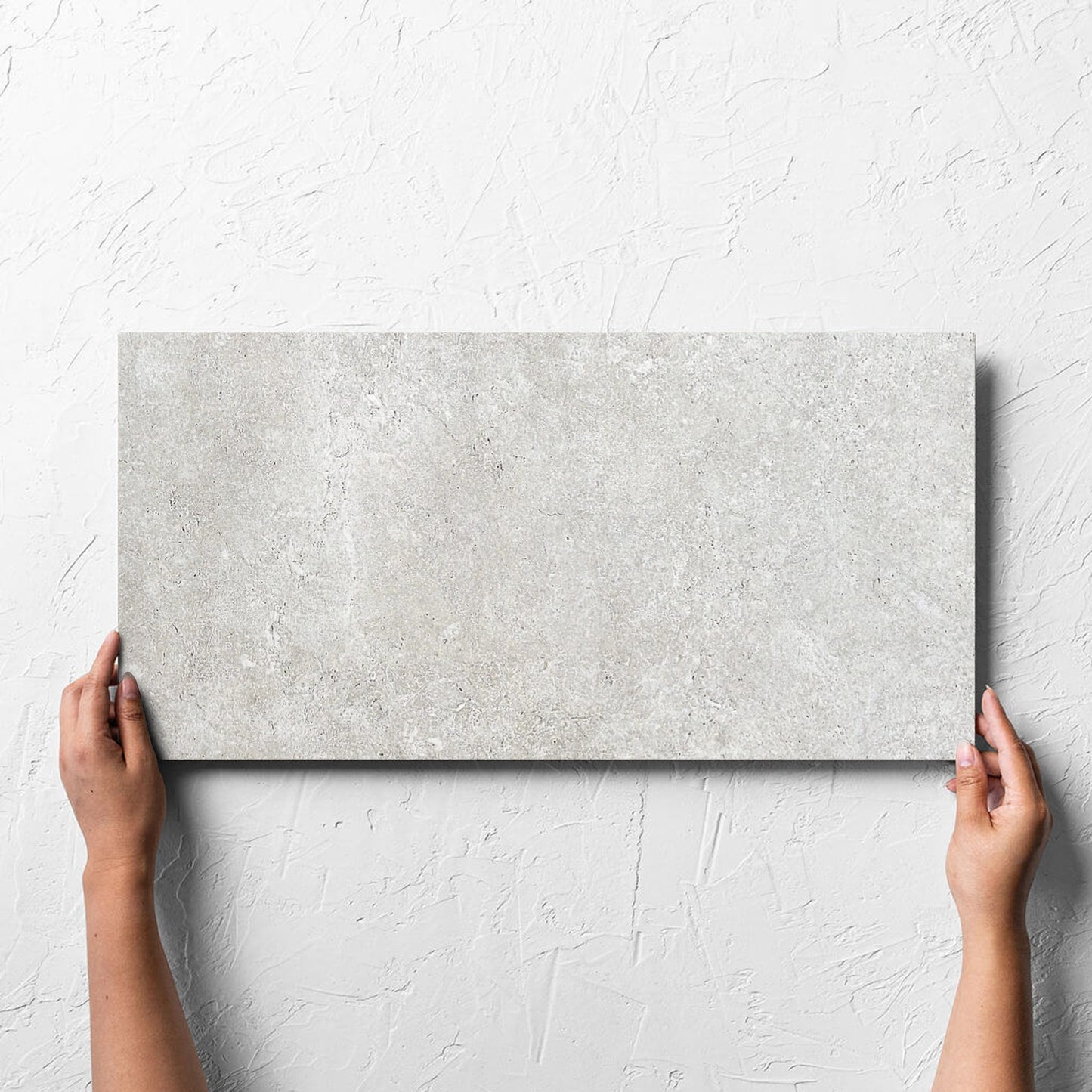 Hand holding a single Stella Ash Matt 300x600mm tile against a white rendered wall, showing the tile surface