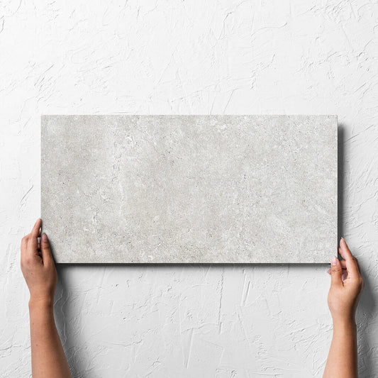 Hand holding a single Stella Ash Matt 300x600mm tile against a white rendered wall, showing the tile surface
