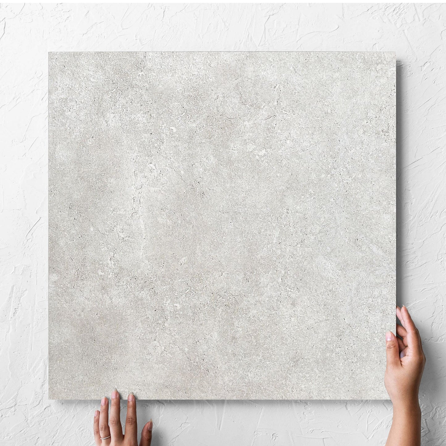 Hand holding a single Stella Ash Matt 600x600mm tile against a white rendered wall, showing the tile surface