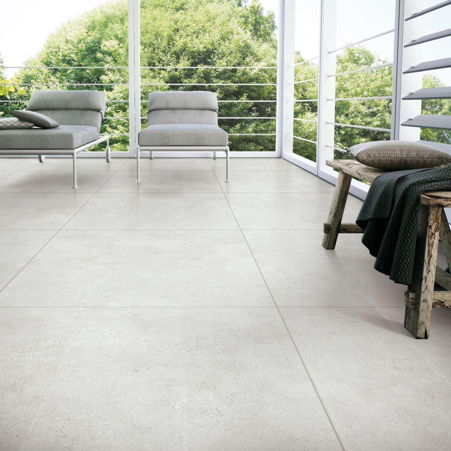 Stella Ash Matt 600x600mm porcelain tiles installed in a bright open-plan living space with modern lounge chairs and floor-to-ceiling windows.