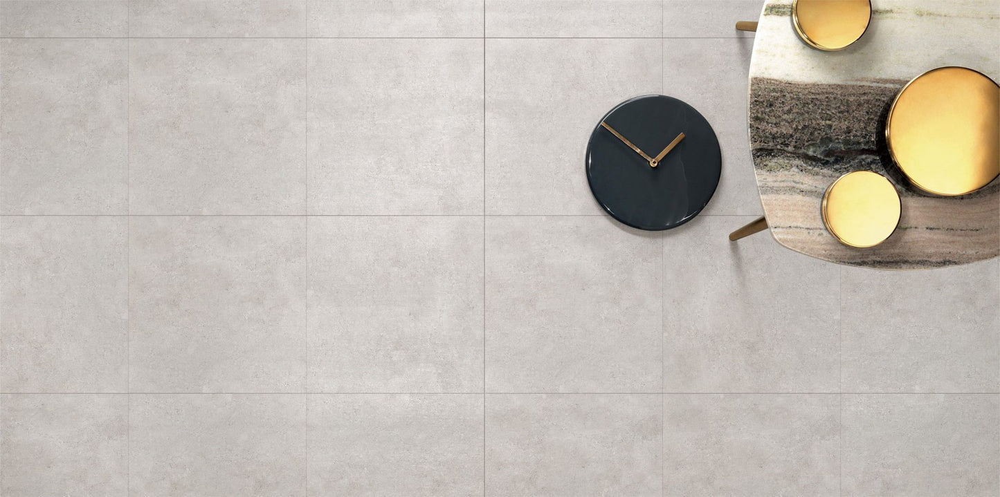 Stella Ash Matt 600x600mm light grey porcelain floor tiles photographed from above with a marble side table, black clock, and gold decorative objects.