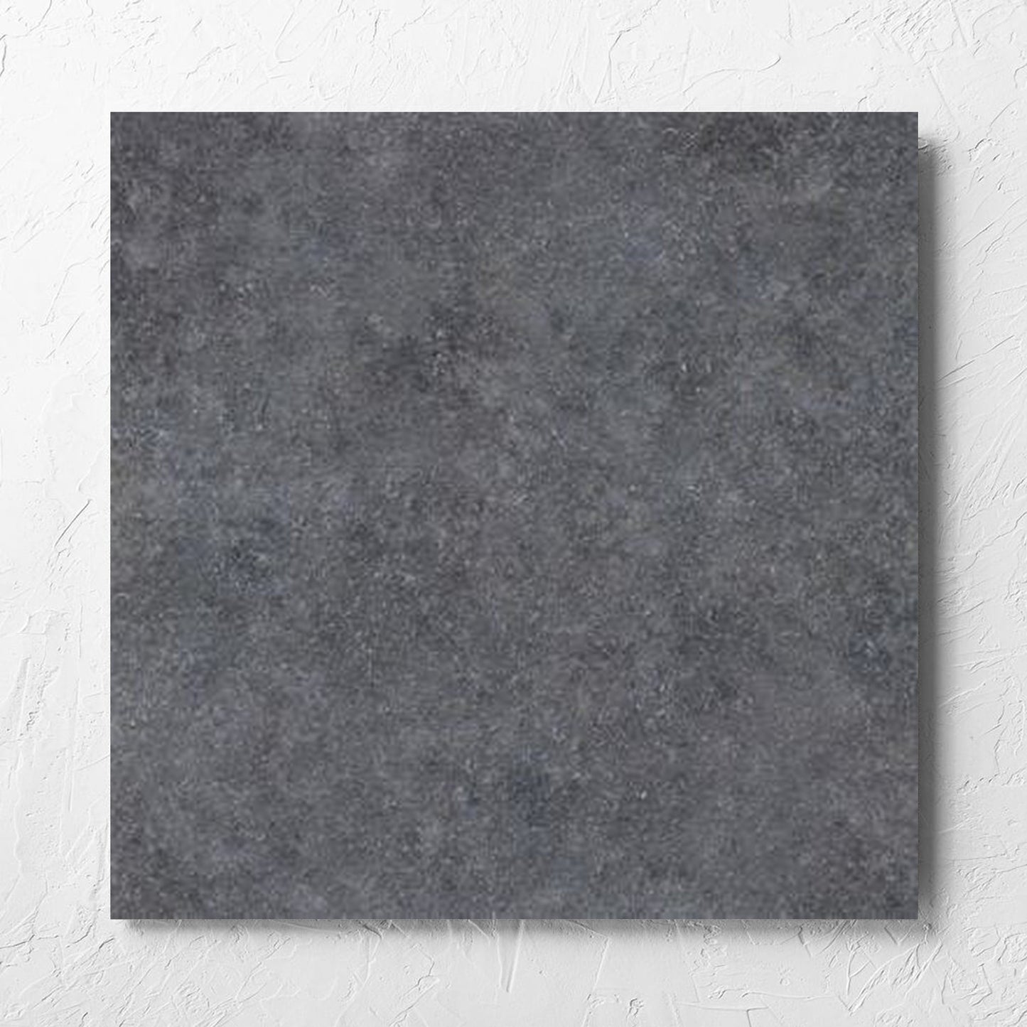 Stella Charcoal Lappato 600x600mm tile laid flat on a white rendered wall, showing the lappato surface