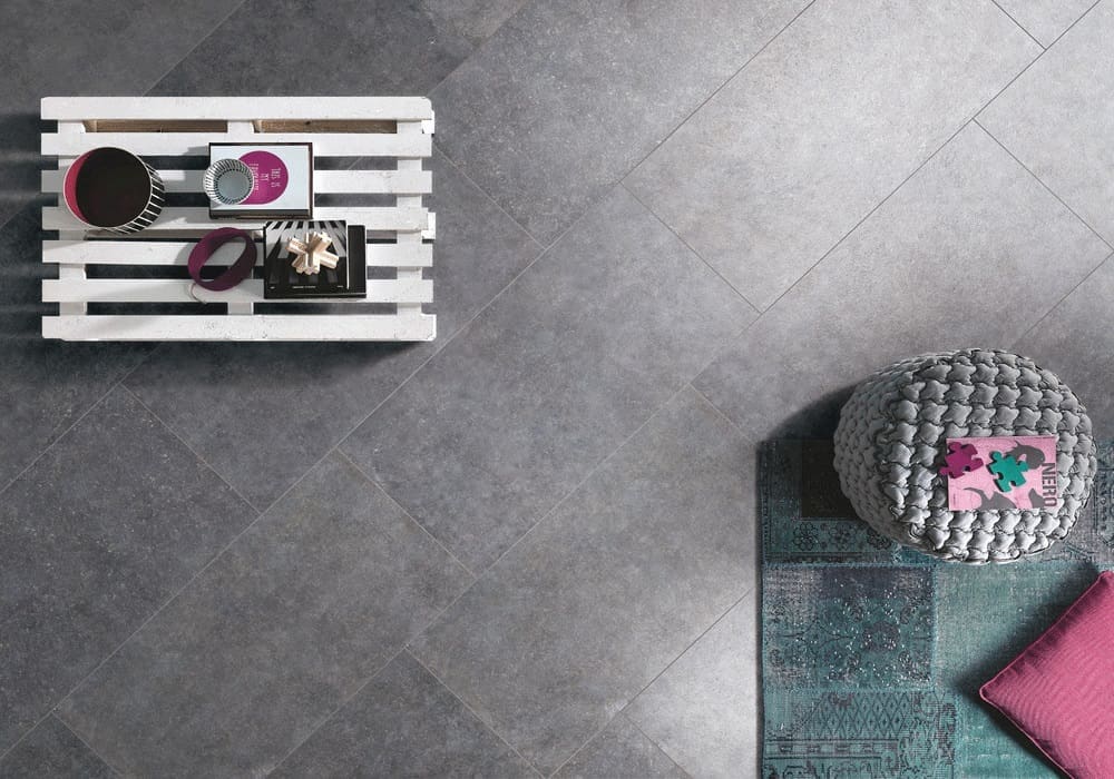 Stella Charcoal Lappato 600x600mm tiles installed as living room floor with a pallet coffee table and woven pouf on a teal rug.