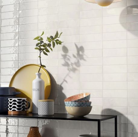 T-Brick Coconut Gloss Subway 52x160mm white ceramic wall tiles installed in a kitchen, styled with colourful bowls, a vase, and decorative accessories on a black shelf.
