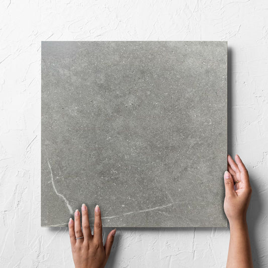 Hand holding a single T-Stone Grey 450x450mm tile against a white rendered wall, showing the tile surface