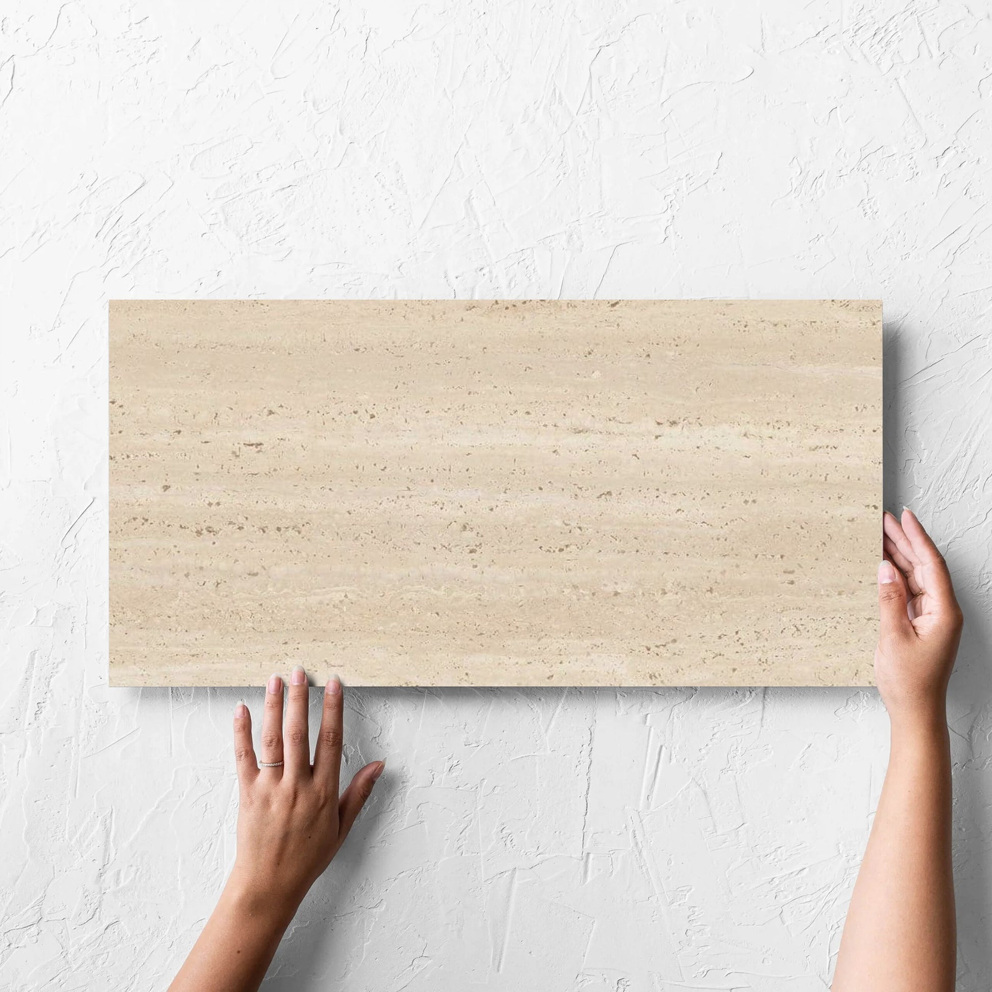 Hand holding a single Tallow Vein Cut Travertine Look Beige 300x600mm tile against a white rendered wall, showing the tile surface
