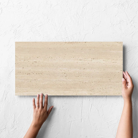 Hand holding a single Tallow Vein Cut Travertine Look Beige 300x600mm tile against a white rendered wall, showing the tile surface