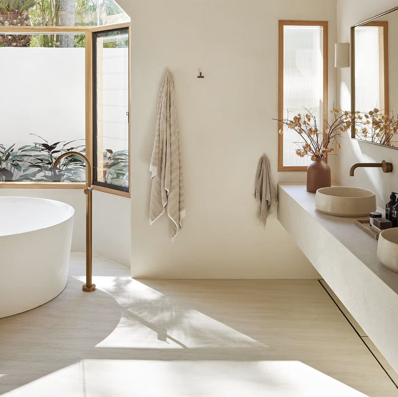 Tallow Vein Cut Travertine Look Ivory 300x600mm tiles on a sunlit bathroom floor paired with a freestanding oval bath, timber-framed windows, and stone vessel sinks.