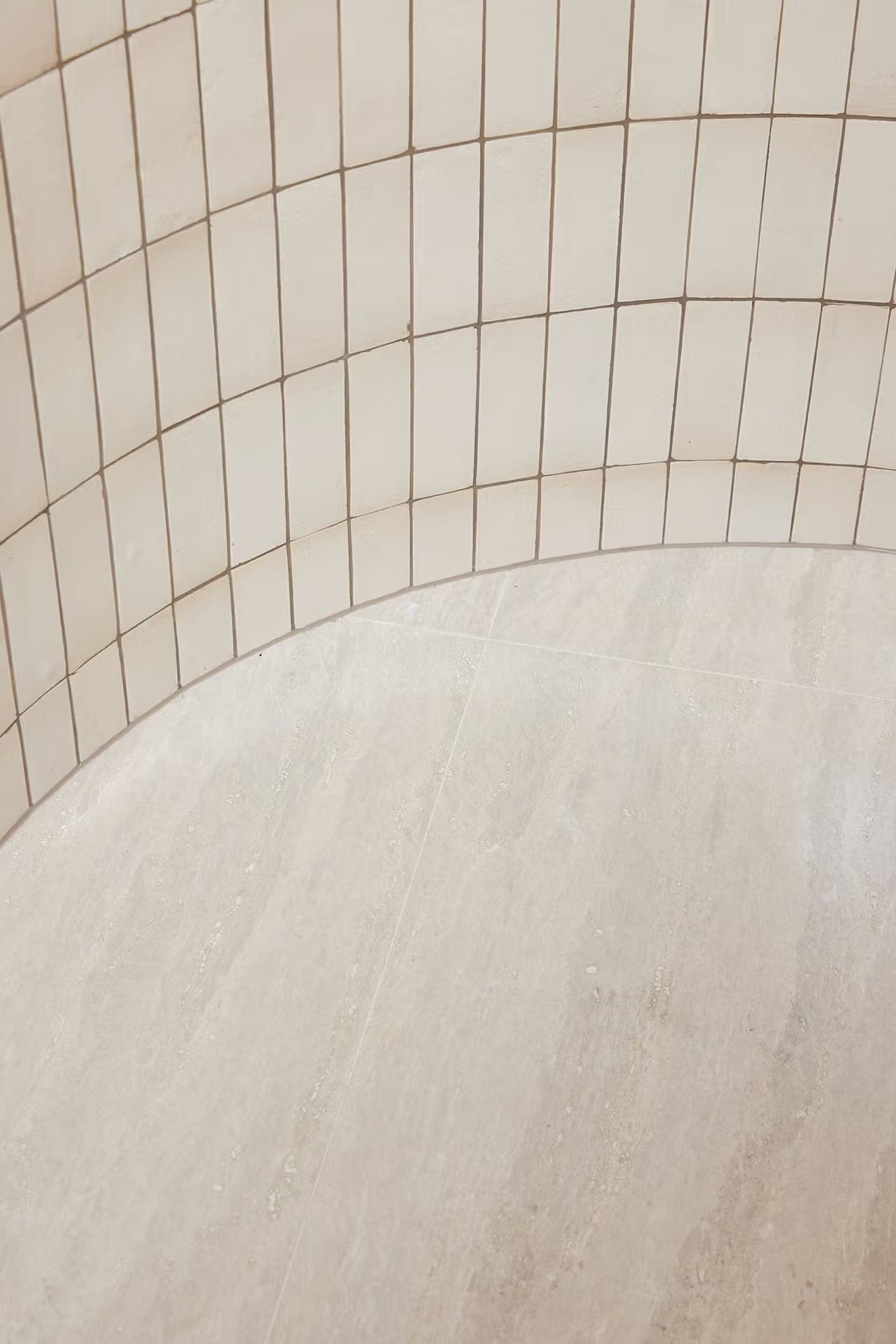 Tallow Vein Cut Travertine Look Ivory 300x600mm tiles installed on a curved shower wall and bench seat in warm cream tones with sandy grout.