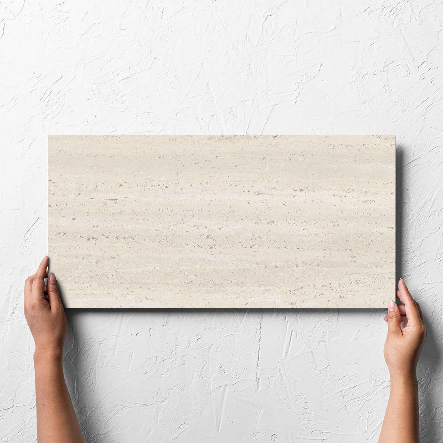 Hand holding a single Tallow Vein Cut Travertine Look Ivory 300x600mm tile against a white rendered wall, showing the tile surface