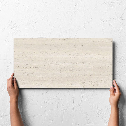 Hand holding a single Tallow Vein Cut Travertine Look Ivory 300x600mm tile against a white rendered wall, showing the tile surface