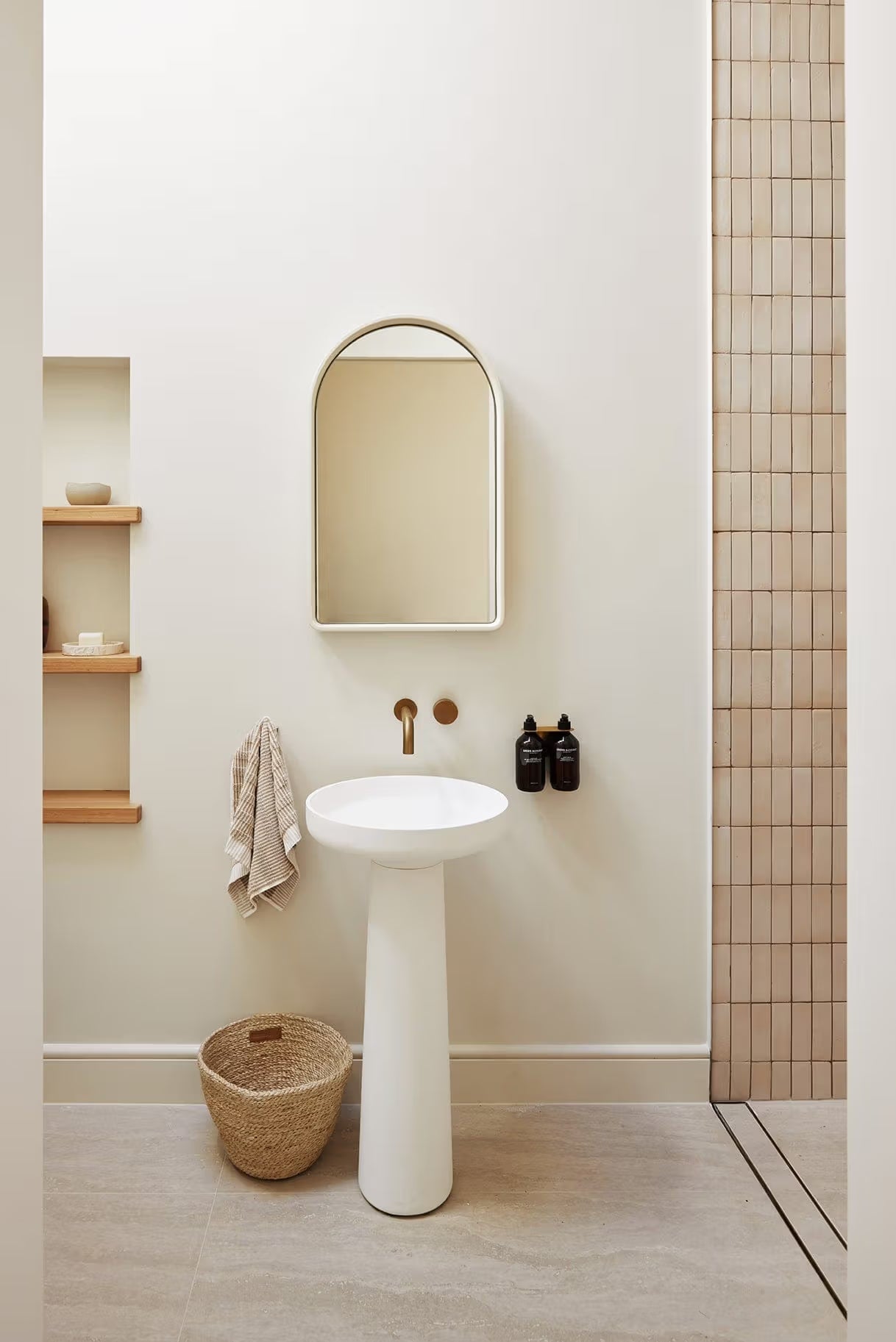 Tallow Vein Cut Travertine Look Ivory 300x600mm tiles installed as a warm beige shower surround beside a white pedestal sink and arched mirror in a minimalist bathroom.