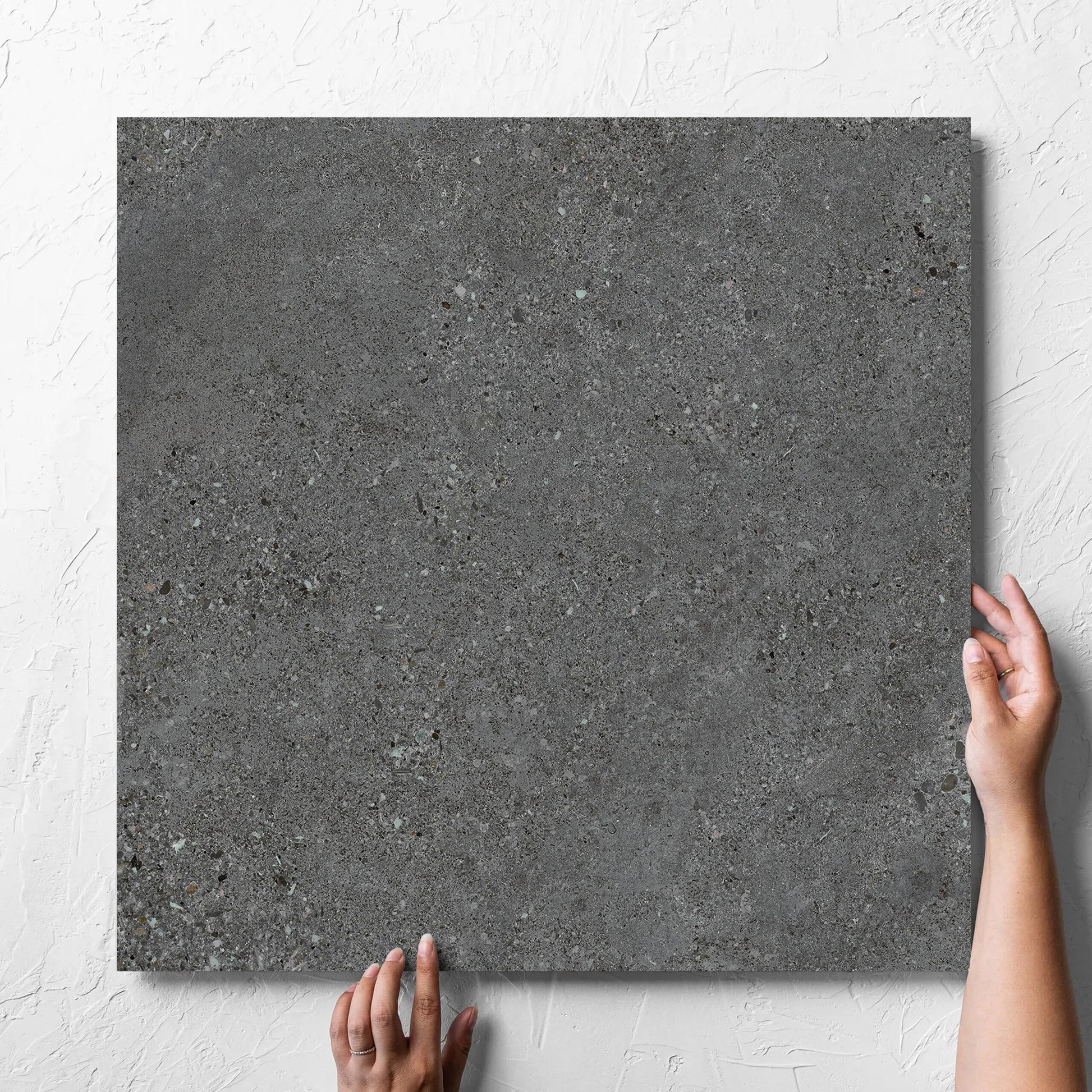 Hand holding a single Terramix Charcoal Lappato 600x600mm tile against a white rendered wall, showing the matt surface