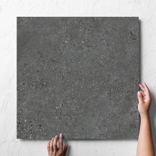 Hand holding a single Terramix Charcoal Lappato 600x600mm tile against a white rendered wall, showing the matt surface