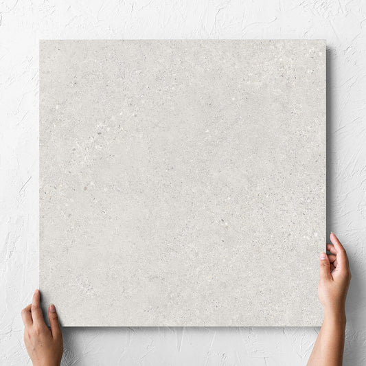Hand holding a single Terramix Cream Grip 600x600mm tile against a white rendered wall, showing the matt surface
