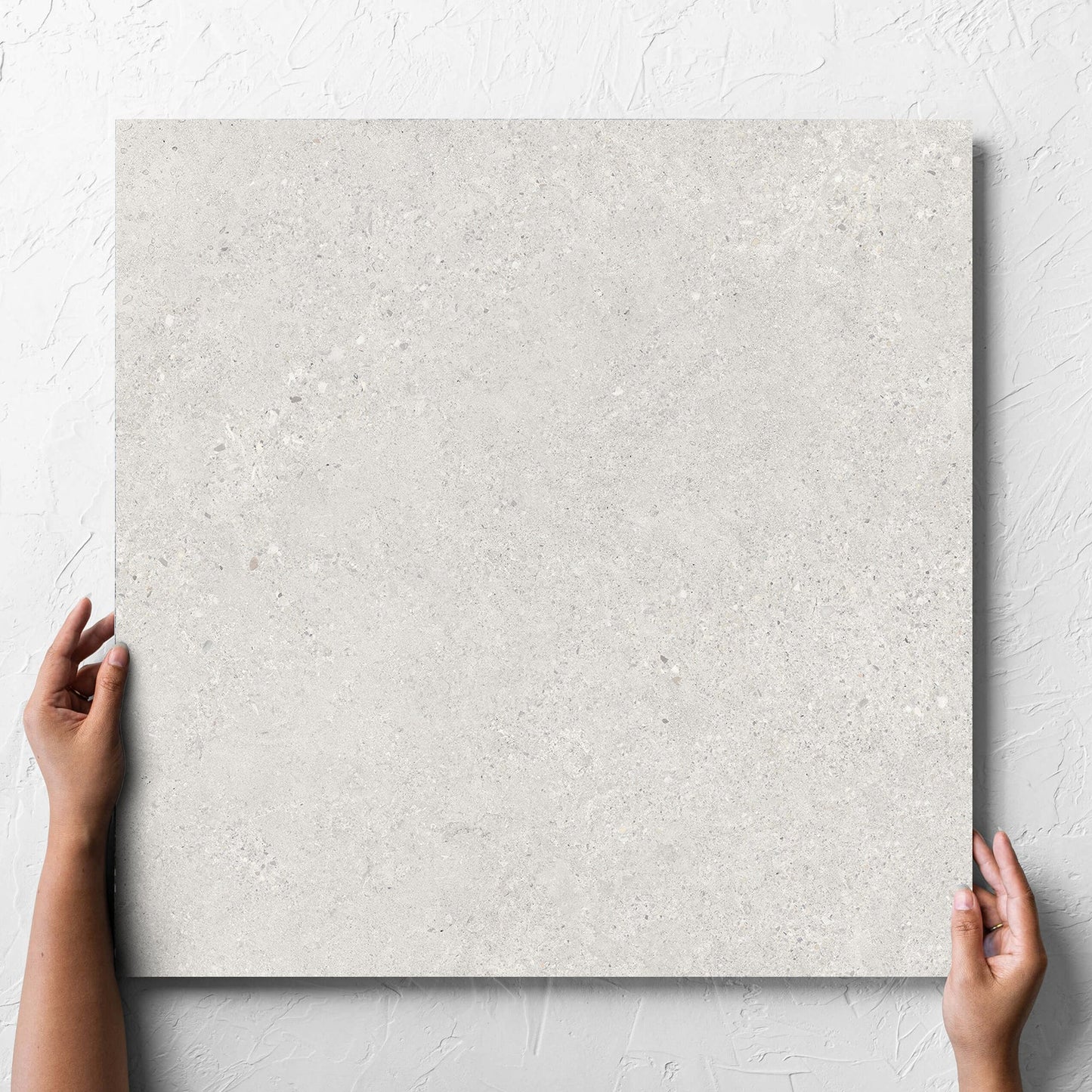 Hand holding a single Terramix Cream Lappato 600x600mm tile against a white rendered wall, showing the matt surface