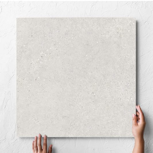 Hand holding a single Terramix Cream Matt 600x600mm tile against a white rendered wall, showing the matt surface
