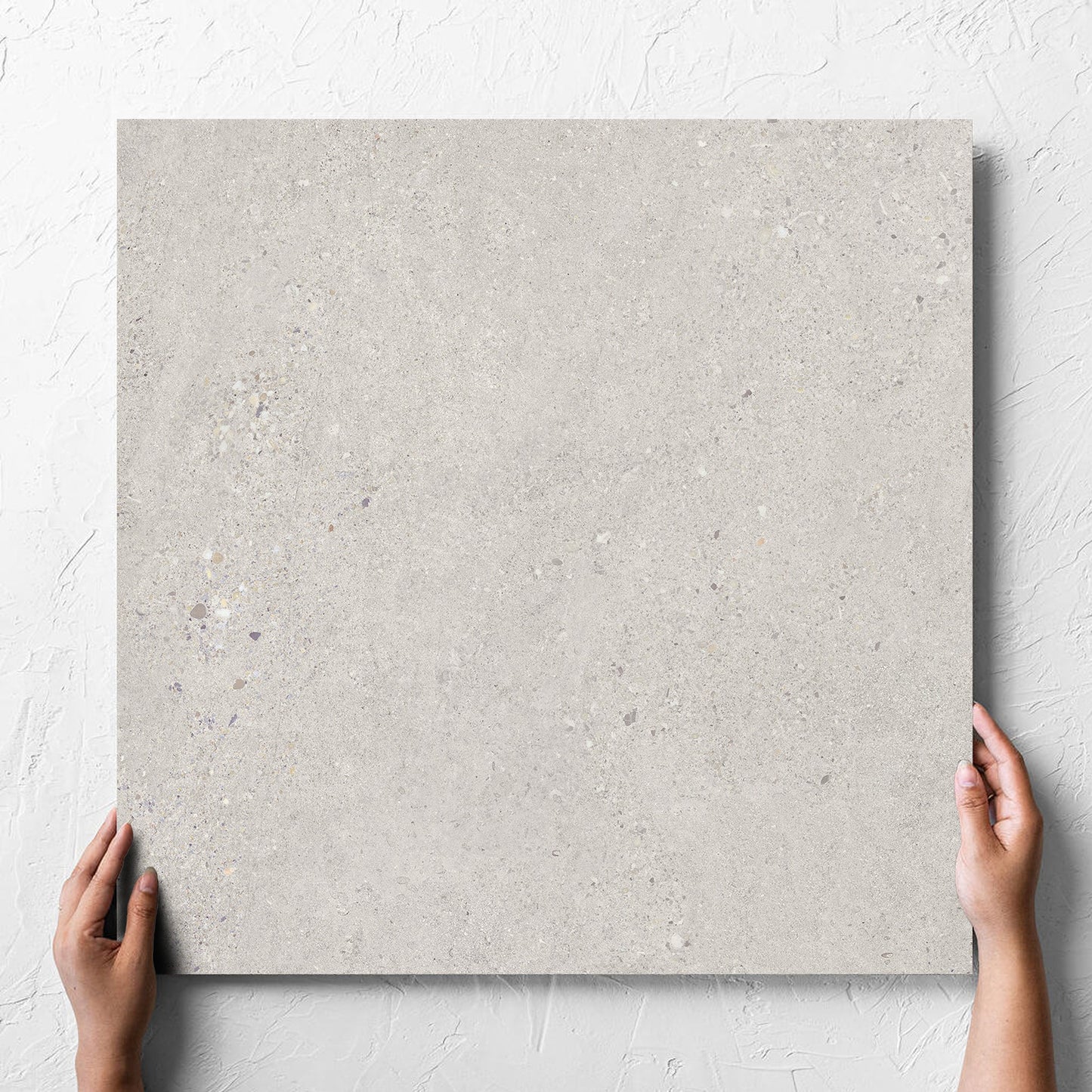 Hand holding a single Terramix Sand Grip 600x600mm tile against a white rendered wall, showing the matt surface