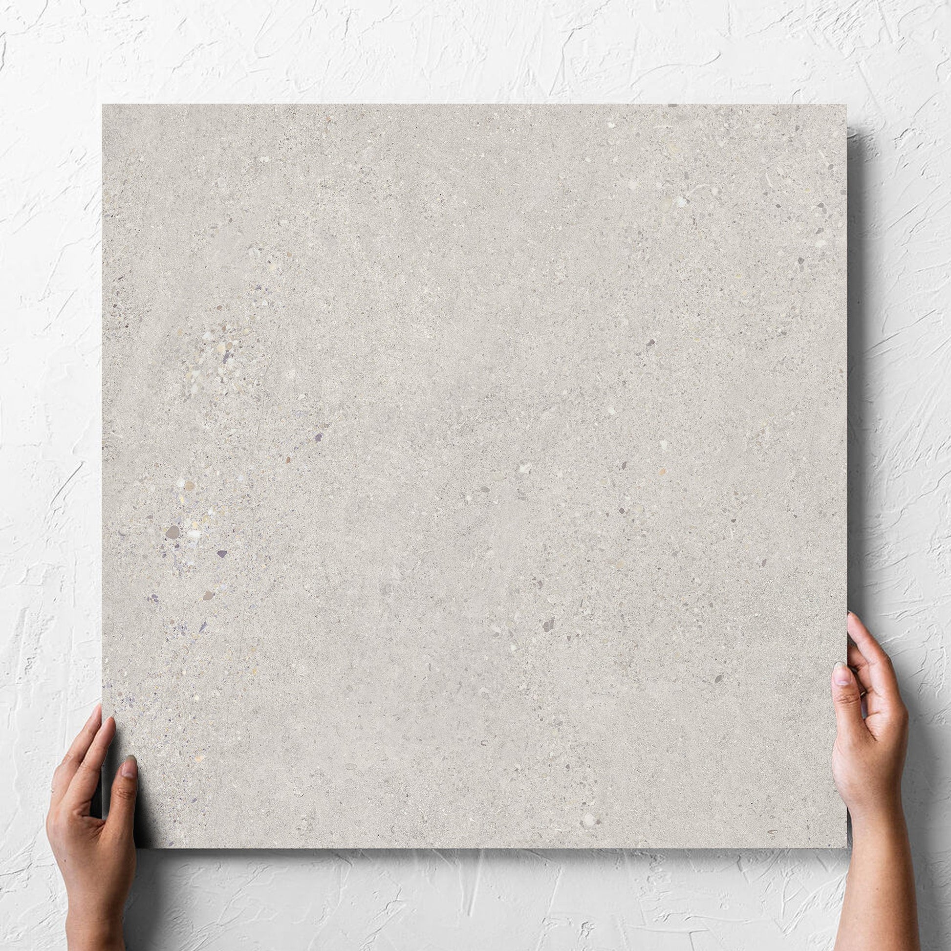Hand holding a single Terramix Sand Grip 600x600mm tile against a white rendered wall, showing the matt surface