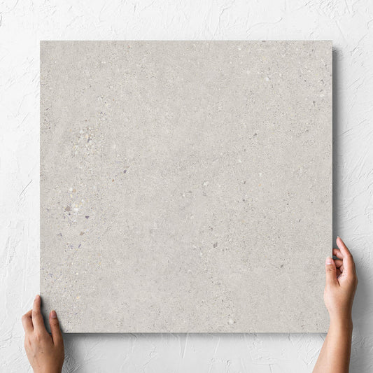 Hand holding a single Terramix Sand Lappato 600x600mm tile against a white rendered wall, showing the matt surface