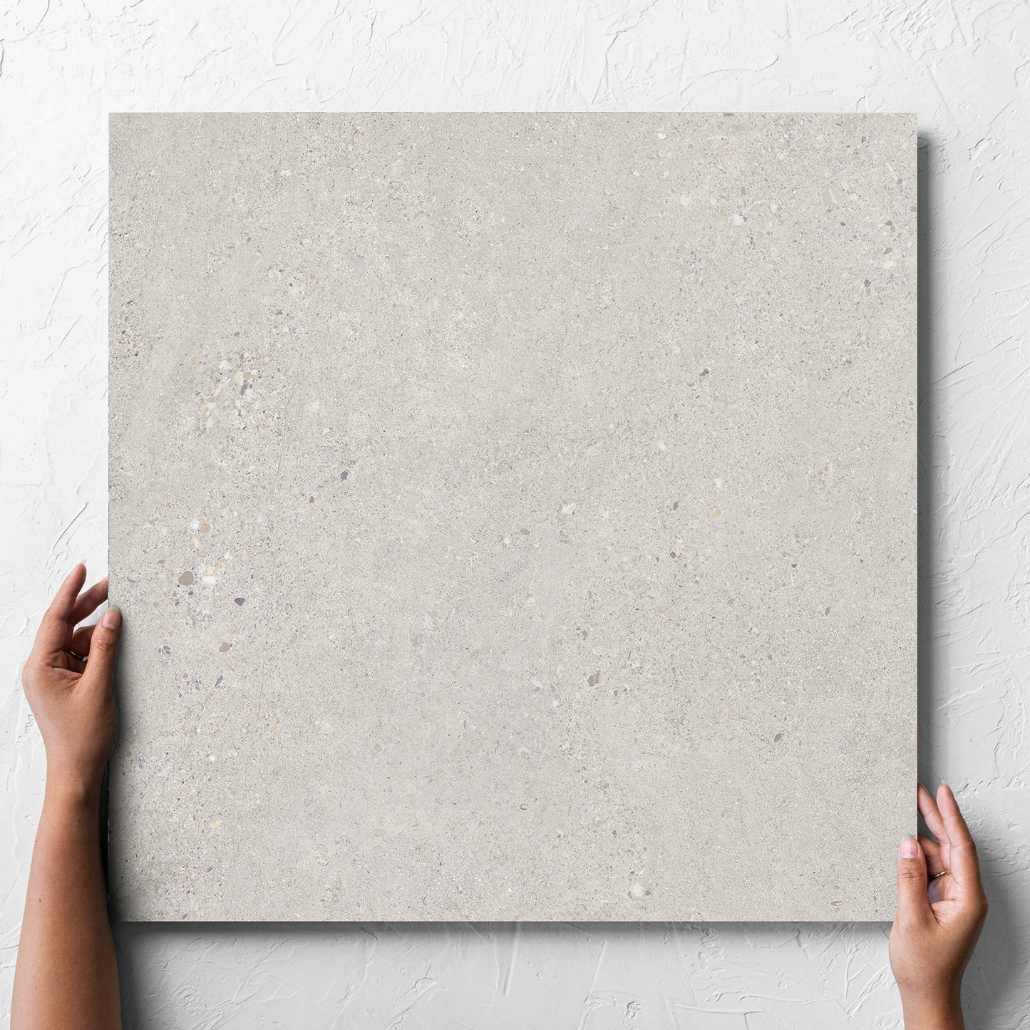 Hand holding a single Terramix Sand Matt 600x600mm tile against a white rendered wall, showing the matt surface