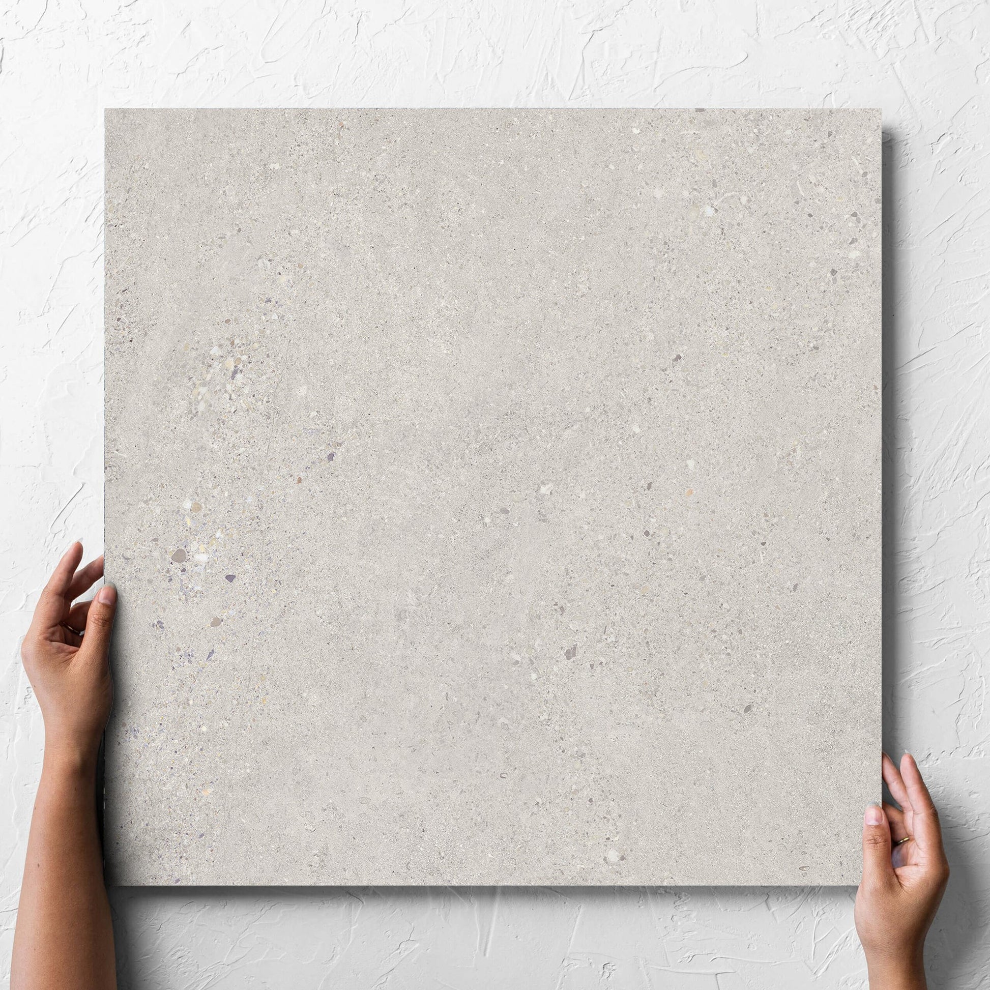 Hand holding a single Terramix Sand Matt 600x600mm tile against a white rendered wall, showing the matt surface