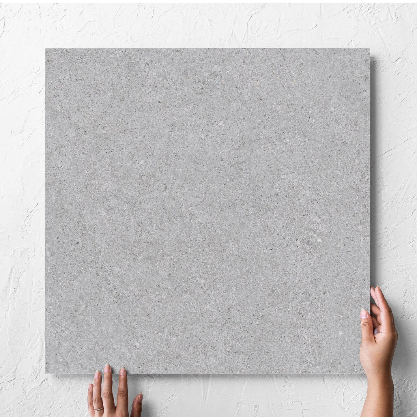 Hand holding a single Terramix Silver Grip 600x600mm tile against a white rendered wall, showing the matt surface