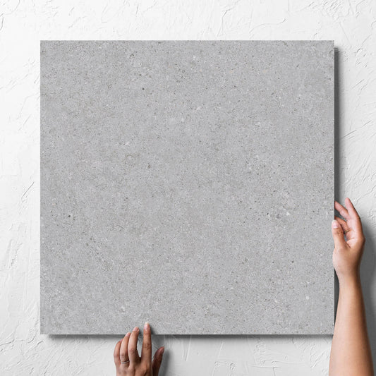 Hand holding a single Terramix Silver Matt 600x600mm tile against a white rendered wall, showing the matt surface
