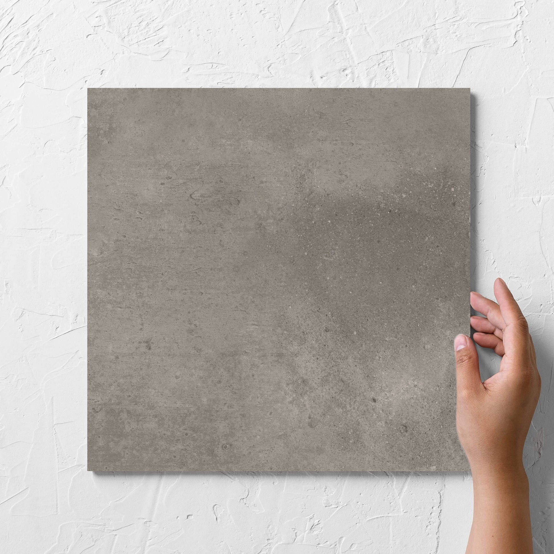 Hand holding a single Thor Mushroom Matt 300x300mm tile against a white rendered wall, showing the matt surface