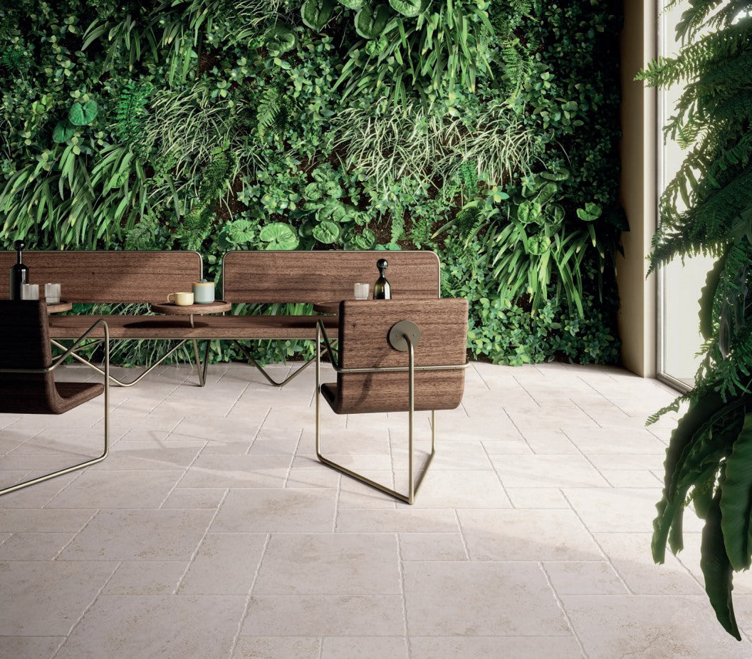 Tibur Bianco Modular 600x600mm cream stone-look floor tiles installed in a biophilic lounge space featuring a living green wall, timber bench seating, and brass-framed chairs.