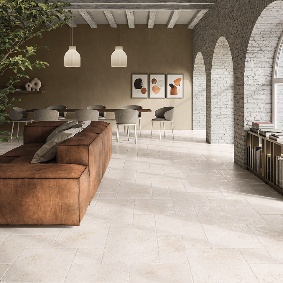Tibur Bianco Modular 600x600mm stone-look floor tiles in an open-plan living and dining room with leather sofa, pendant lights, and arched brick walls.