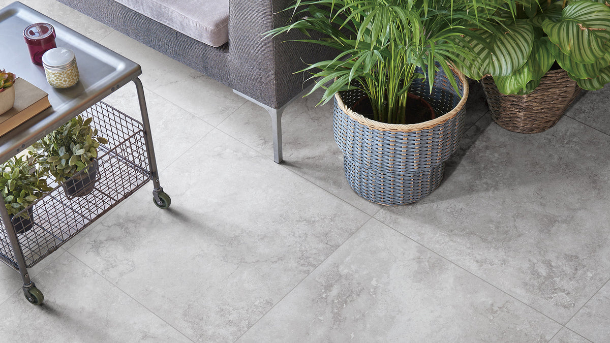 Timeless Silver Structured 600x600mm tiles installed as a living room floor, styled with wicker planters, lush green plants, and an industrial metal trolley.